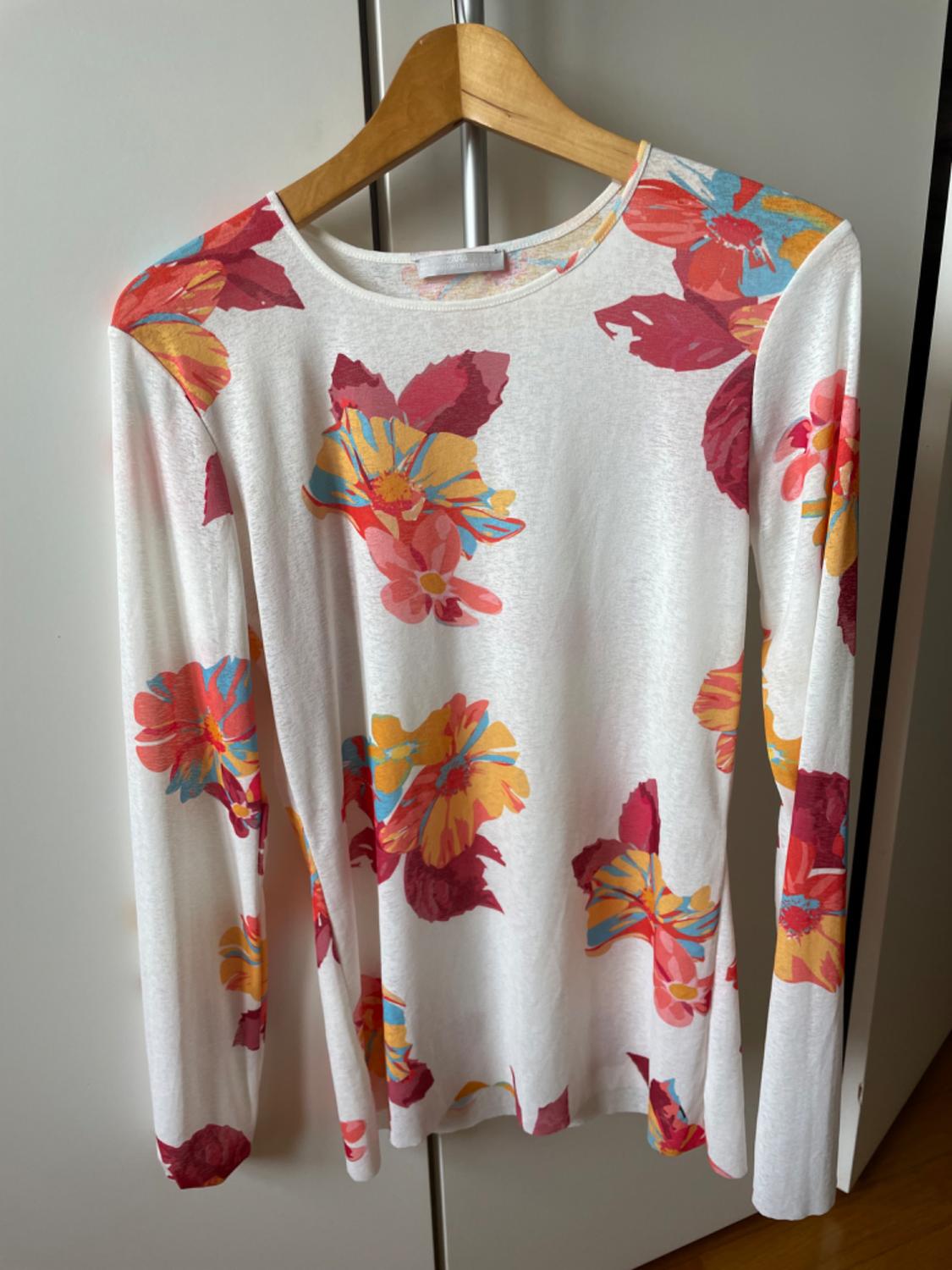 Front view of a white t-shirt with a floral print in shades of red, yellow, and blue, long sleeves.