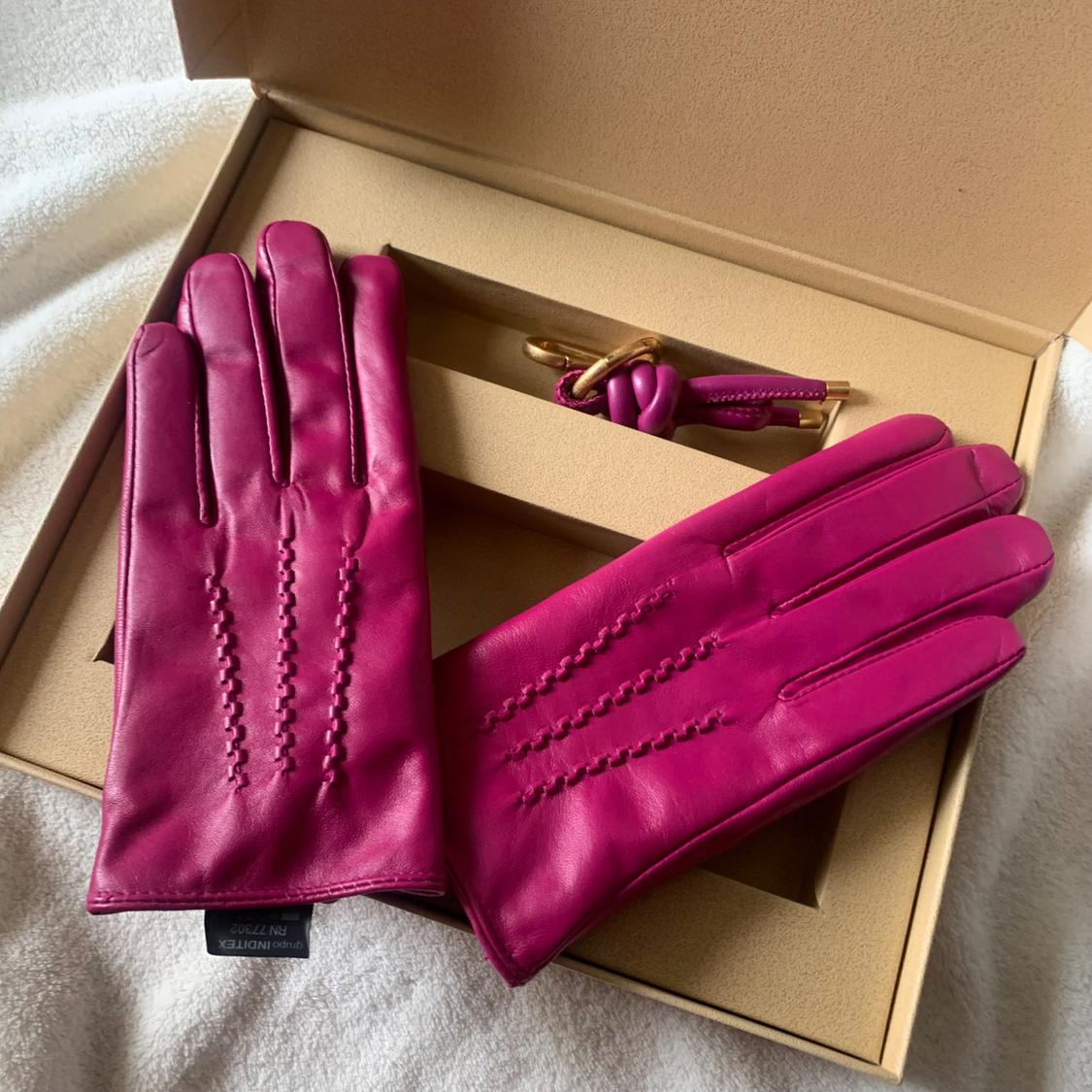 Pink leather gloves with decorative stitching, presented in a beige box alongside a gold and pink keyring.