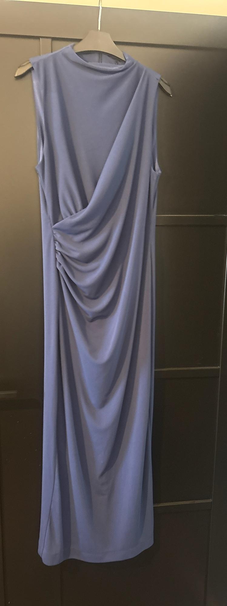 Blue sleeveless maxi dress with a high neck and side draping, hanging on a black hanger in front of a dark door.