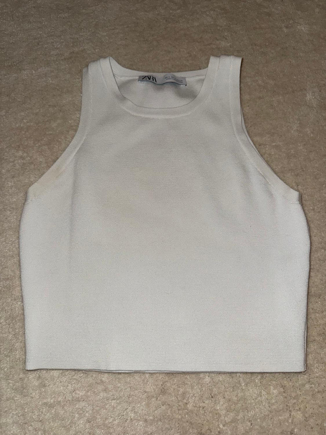 White sleeveless top on a beige background, visible label with text "ZARA".