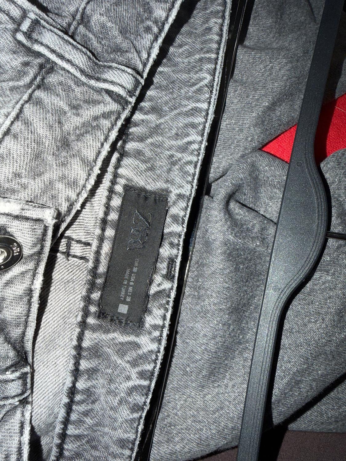 Black label on textured grey trousers, against a grey and red fabric background. Visible text: "MADE IN ITALY".