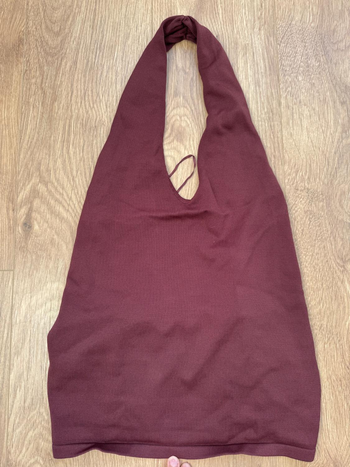Burgundy sleeveless top on light wooden flooring. Design with a halter neckline and ribbed texture.