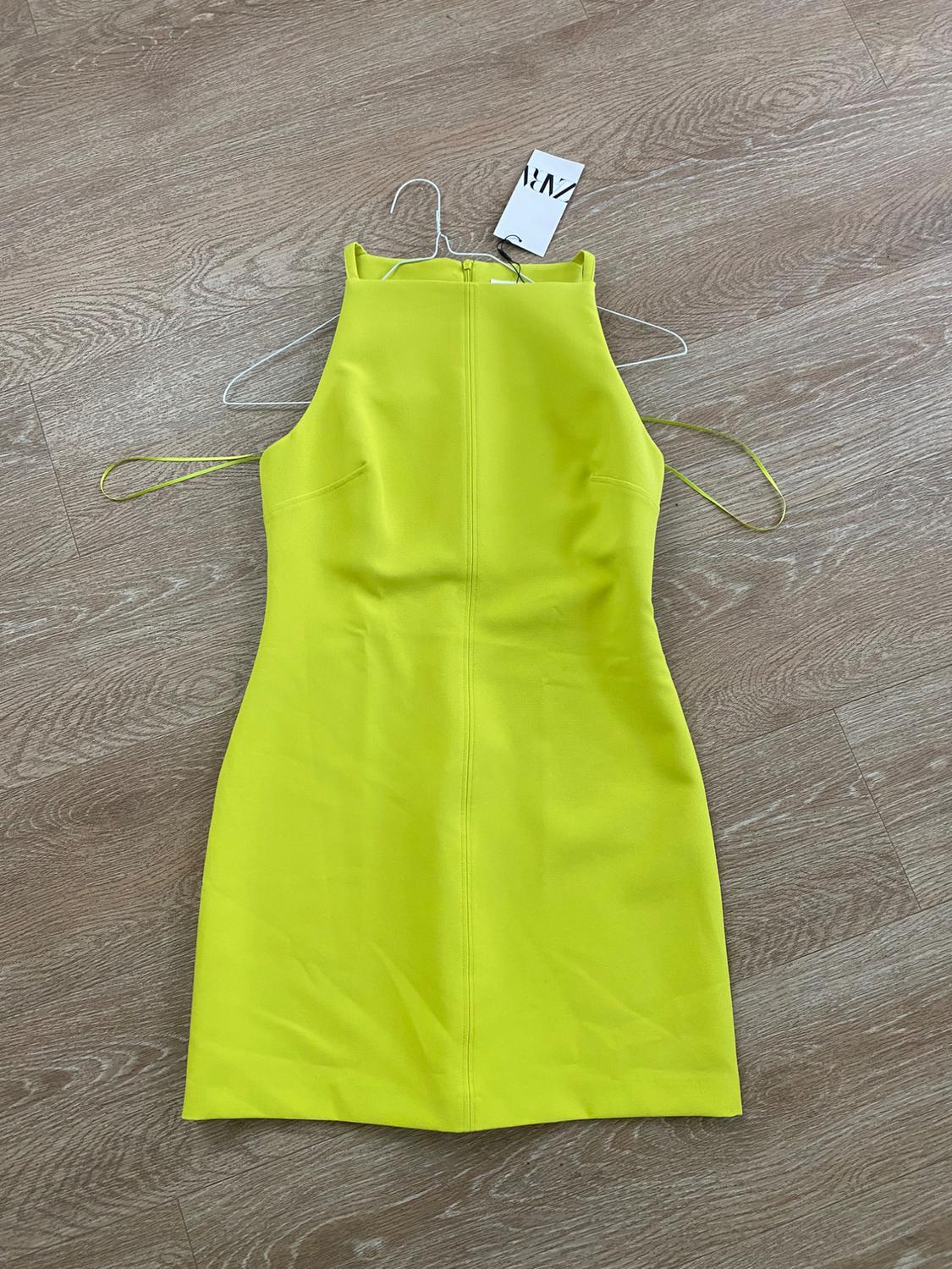 Neon yellow sleeveless dress on a wooden floor, hanging on a hanger with a visible tag.
