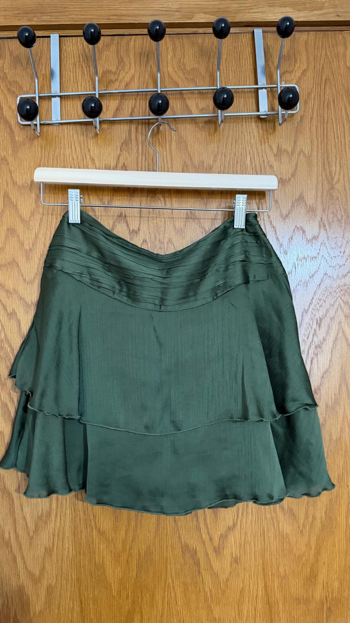 Dark green satin-fabric miniskirt with frills, hanging on a hanger over a wooden door.