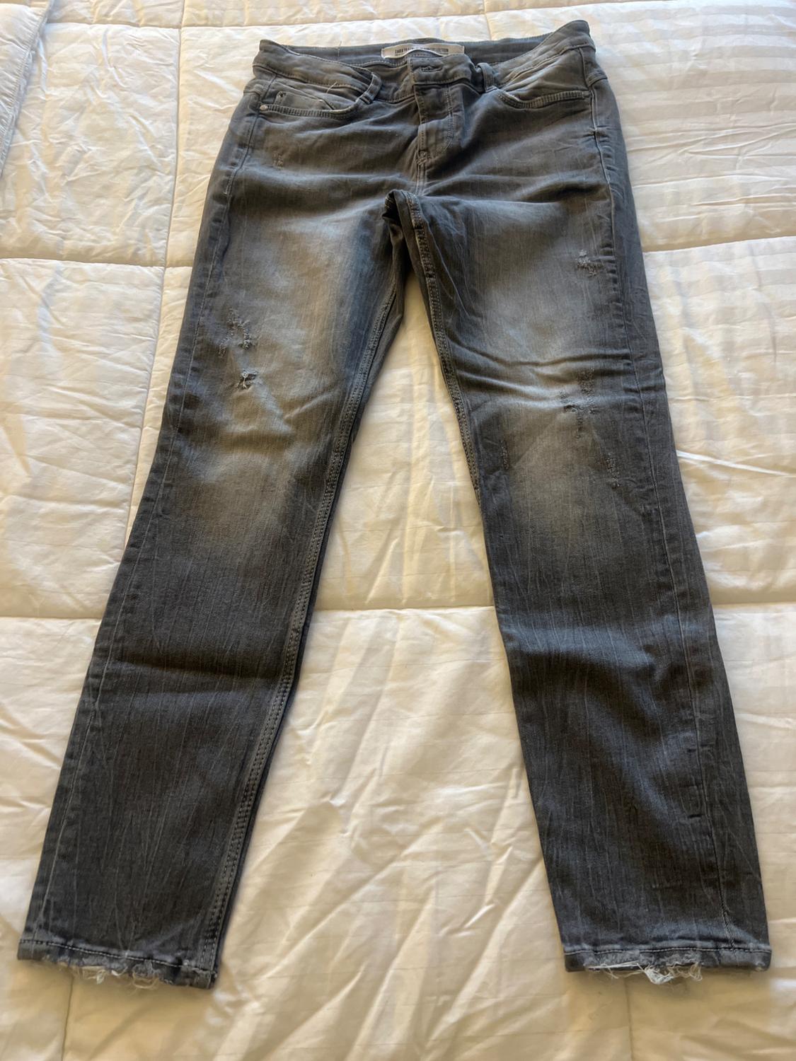 Front view of grey denim jeans with front pockets and distressed details.