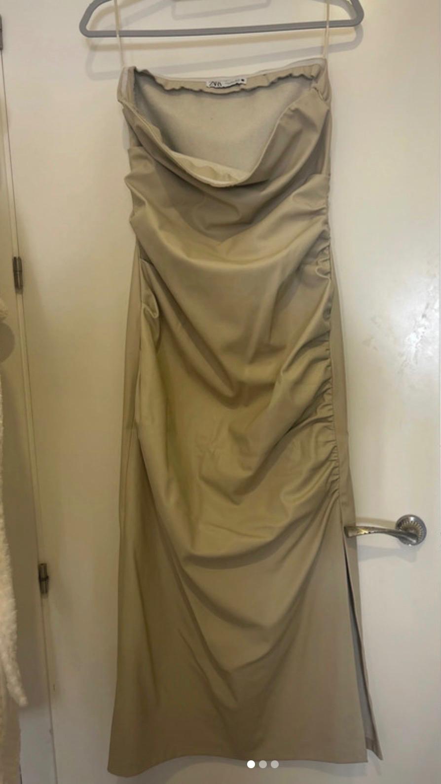 Beige draped dress hanging on a white hanger over a white door. Visible label on the inside of the dress.