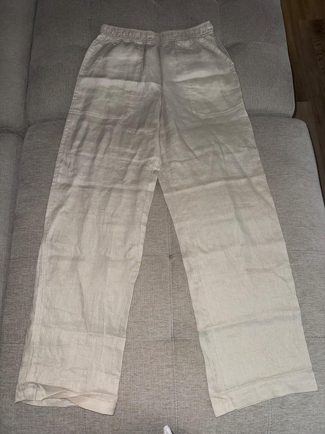 Beige linen pants with elastic waistband and side pockets, placed on a gray sofa.