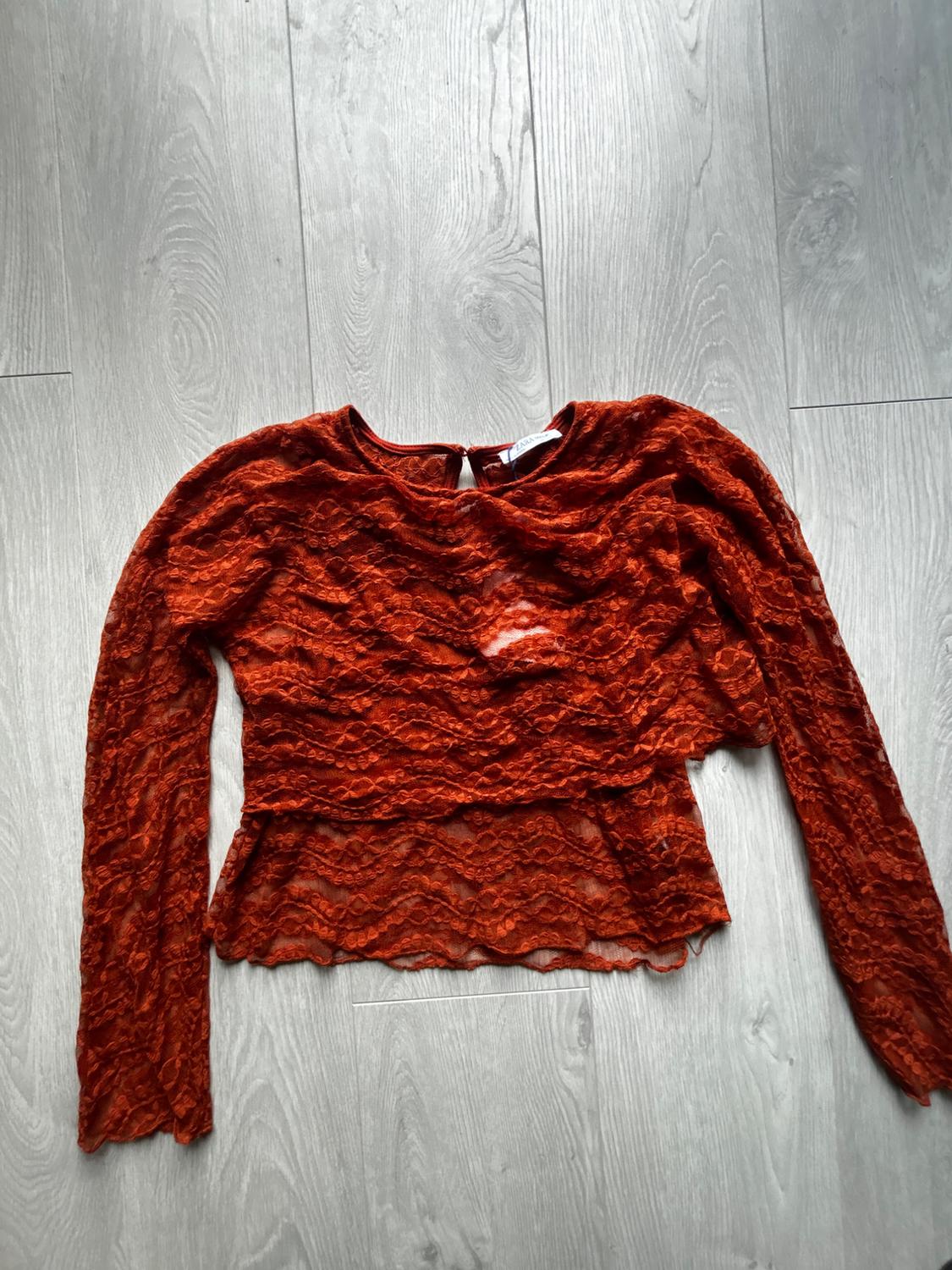 Dark orange semi-sheer lace long-sleeved top, on a grey wooden floor. The neck label reads ZARA.