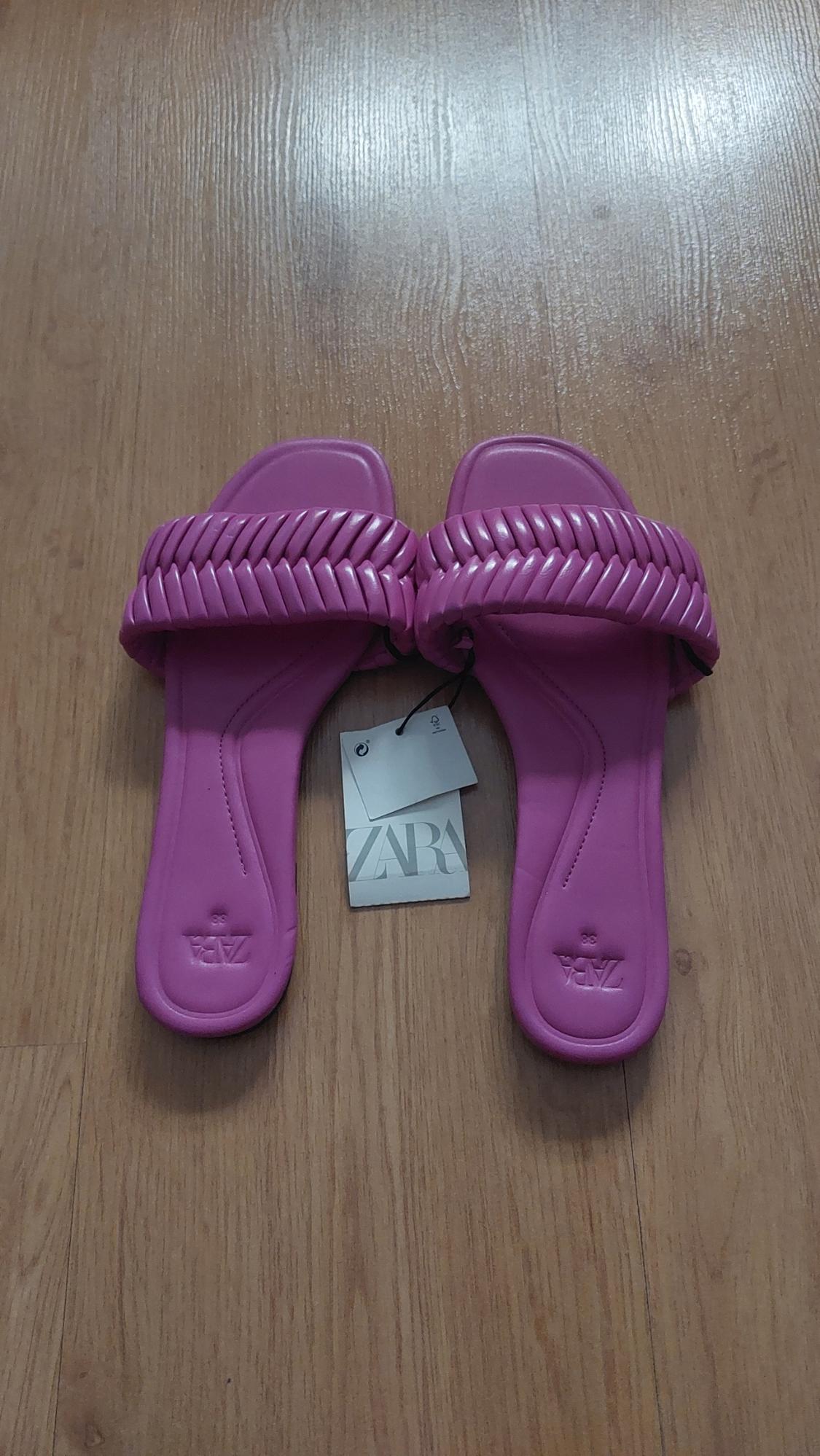Fuchsia sandals with a braided design on a wooden floor. Visible label with the text "ZARA".