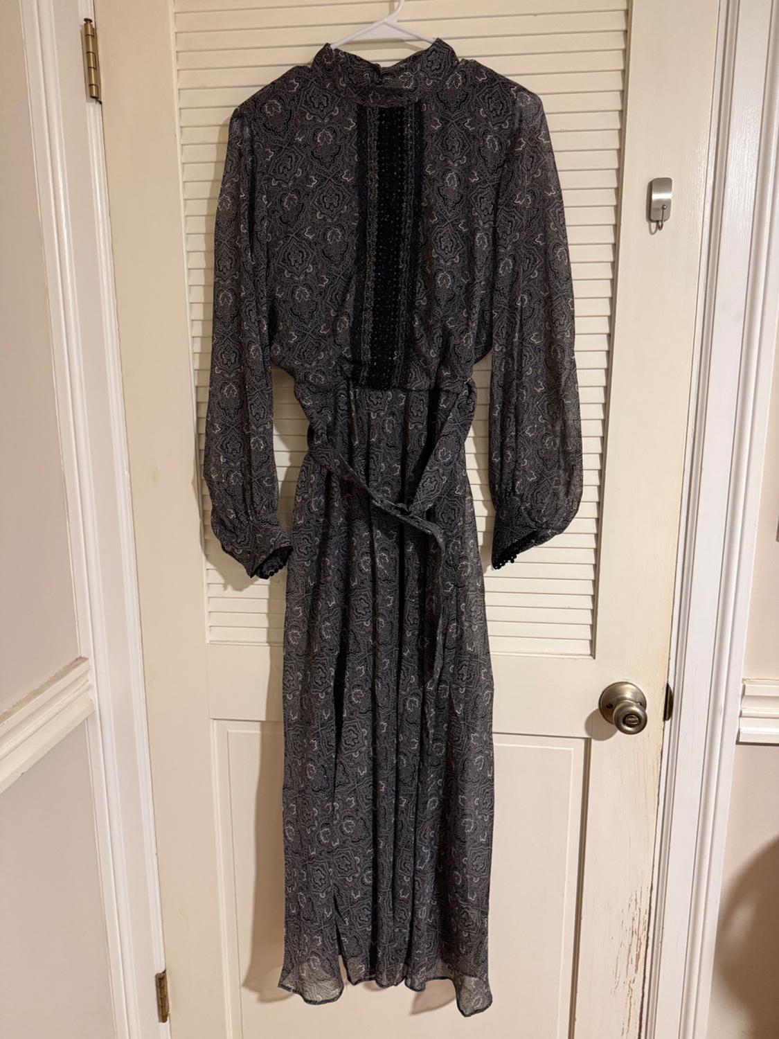 Printed long dress in dark tones hanging on a white door. Long sleeves and matching belt.