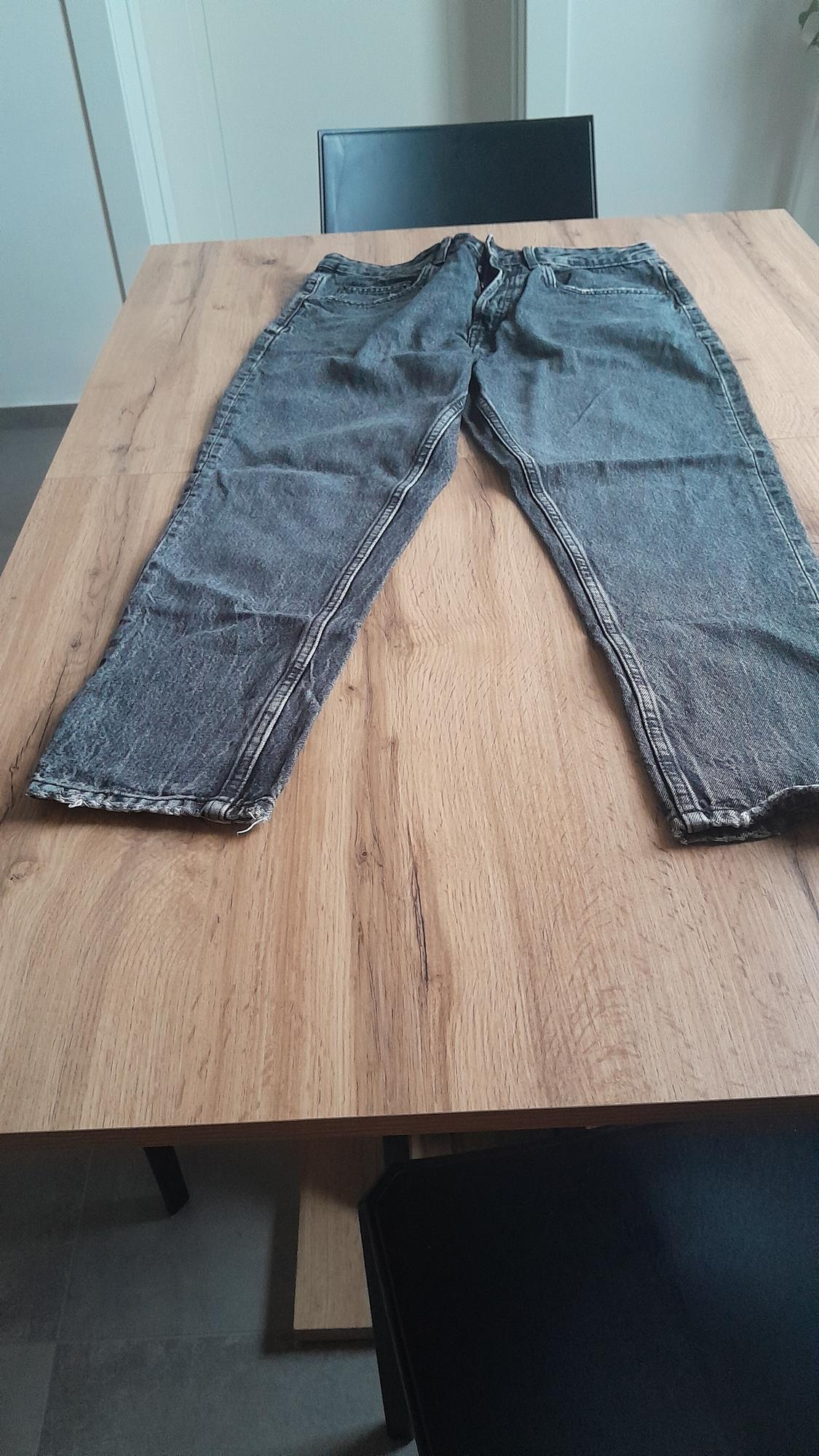 Dark grey distressed jeans on a light wooden table in a minimalist indoor setting.
