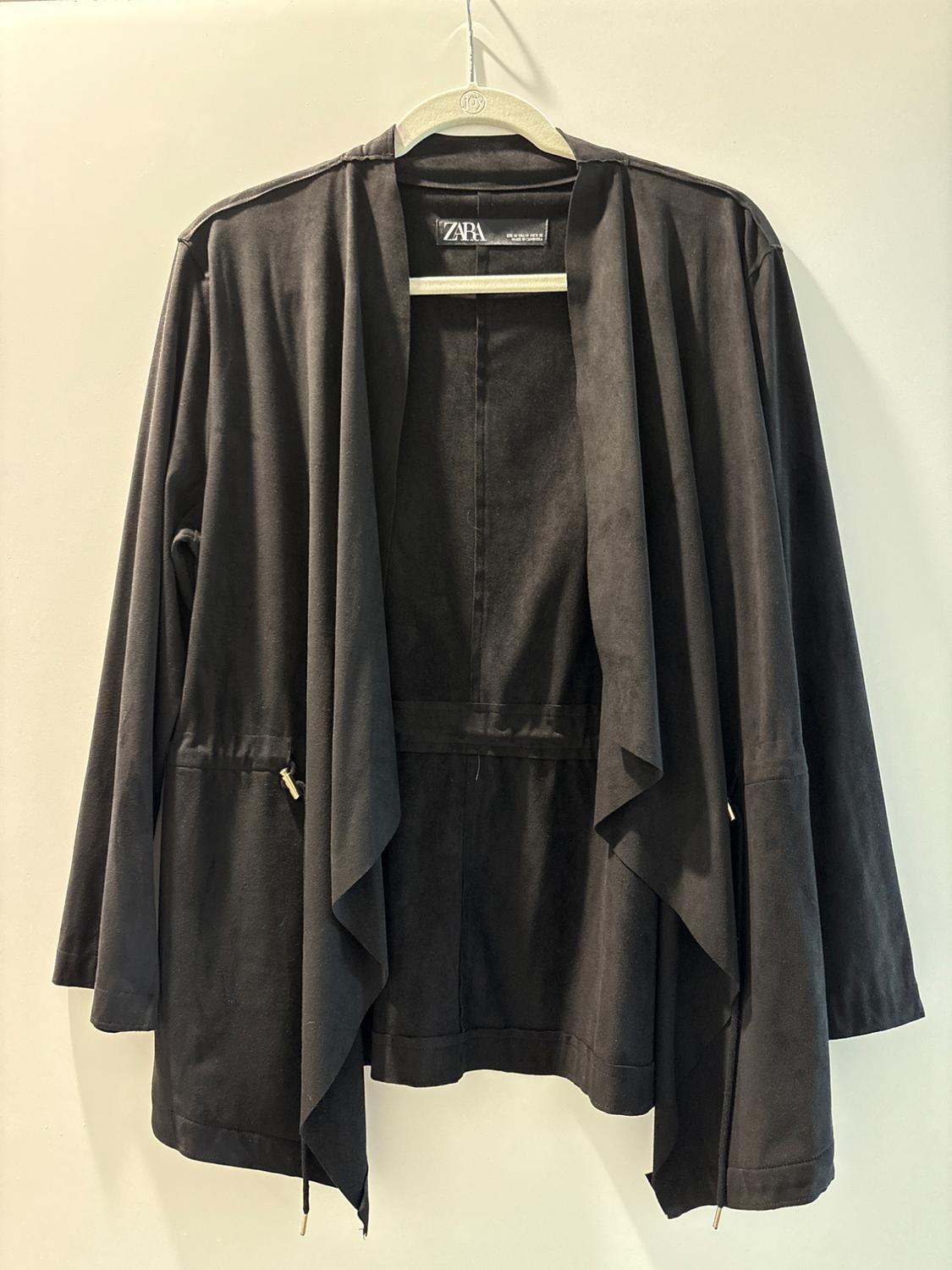Black jacket hanging on a wooden hanger, with visible Zara label, plain white background.