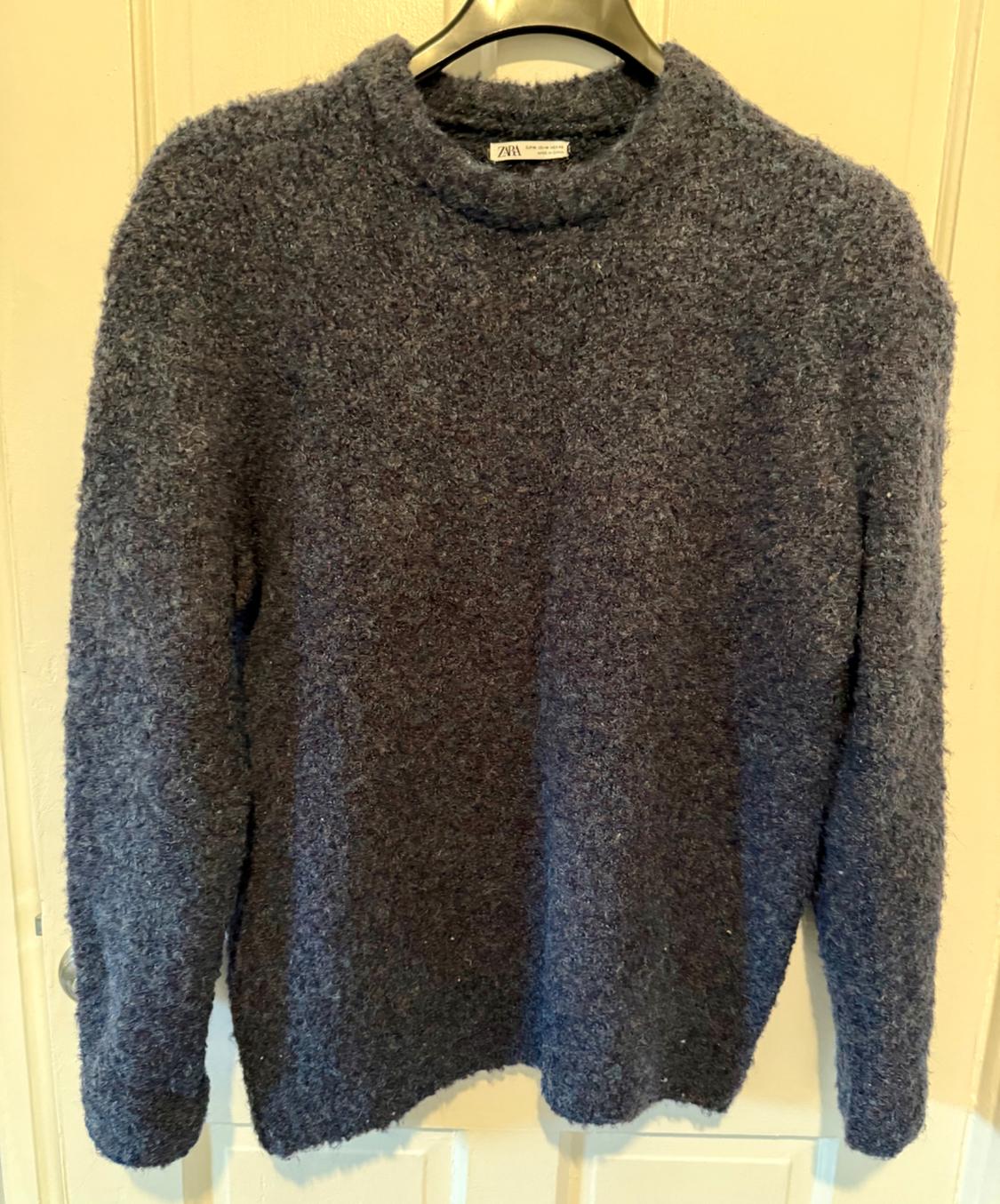 Textured grey jumper hanging on a hanger over a white door. Label visible on the collar.