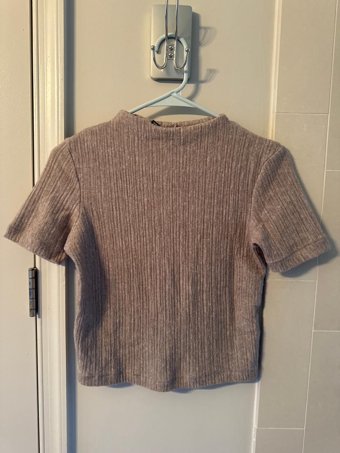 Grey ribbed short-sleeved t-shirt hanging on a blue hanger against a light-coloured wall.