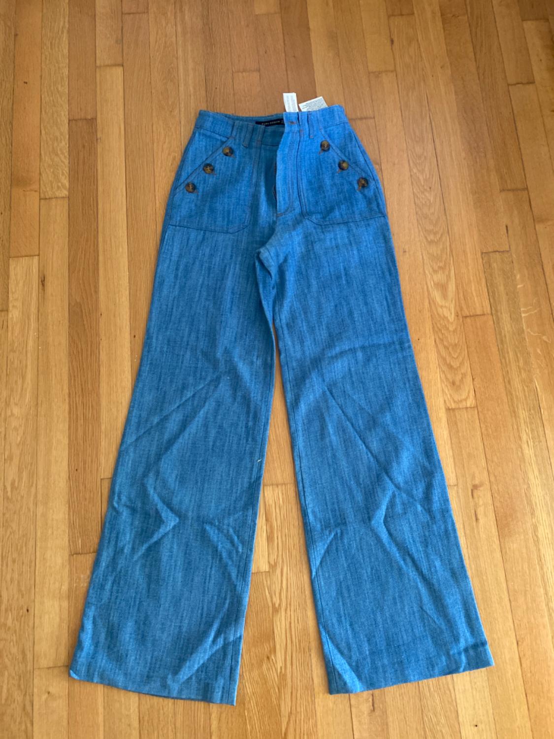 Front view of blue trousers with brown buttons and side pockets.
