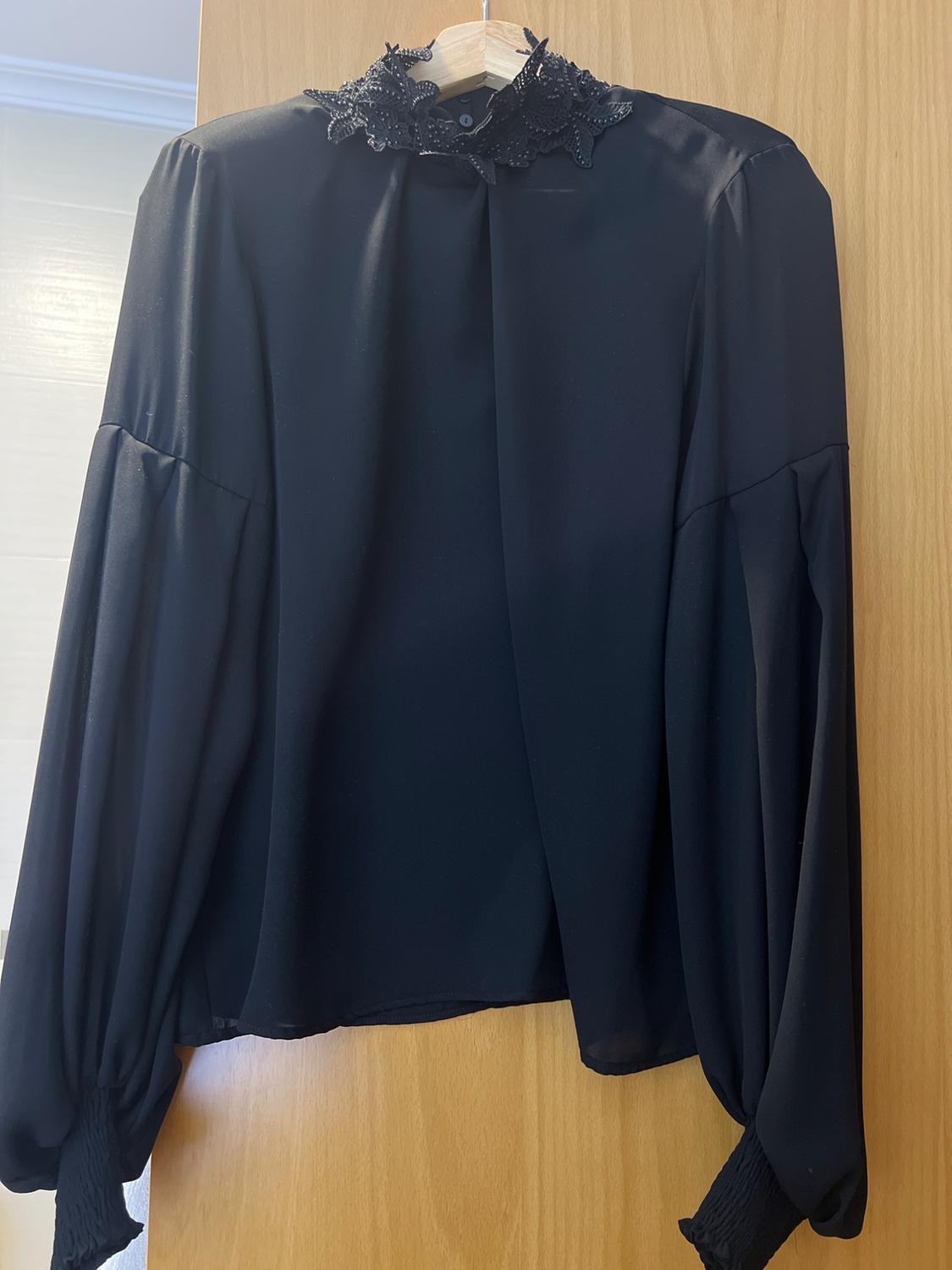 Front view of a black blouse with an embroidered collar and long puffed sleeves.