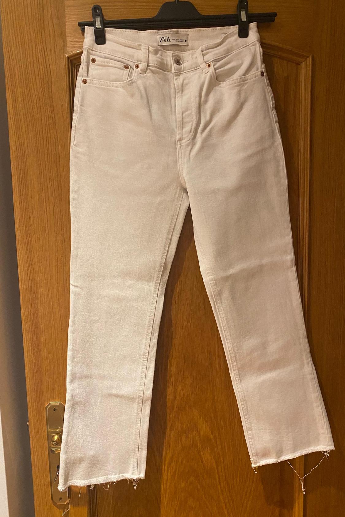 Front view of white trousers with five pockets and frayed hems.