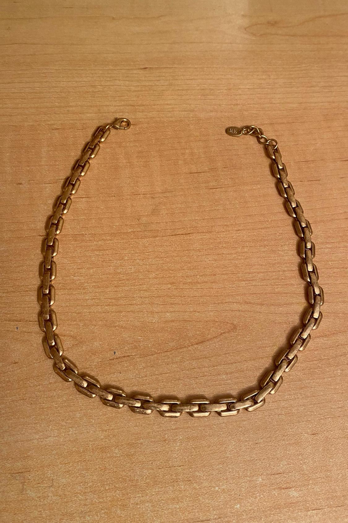 Gold chain with large links and hook clasp on a light wood background.