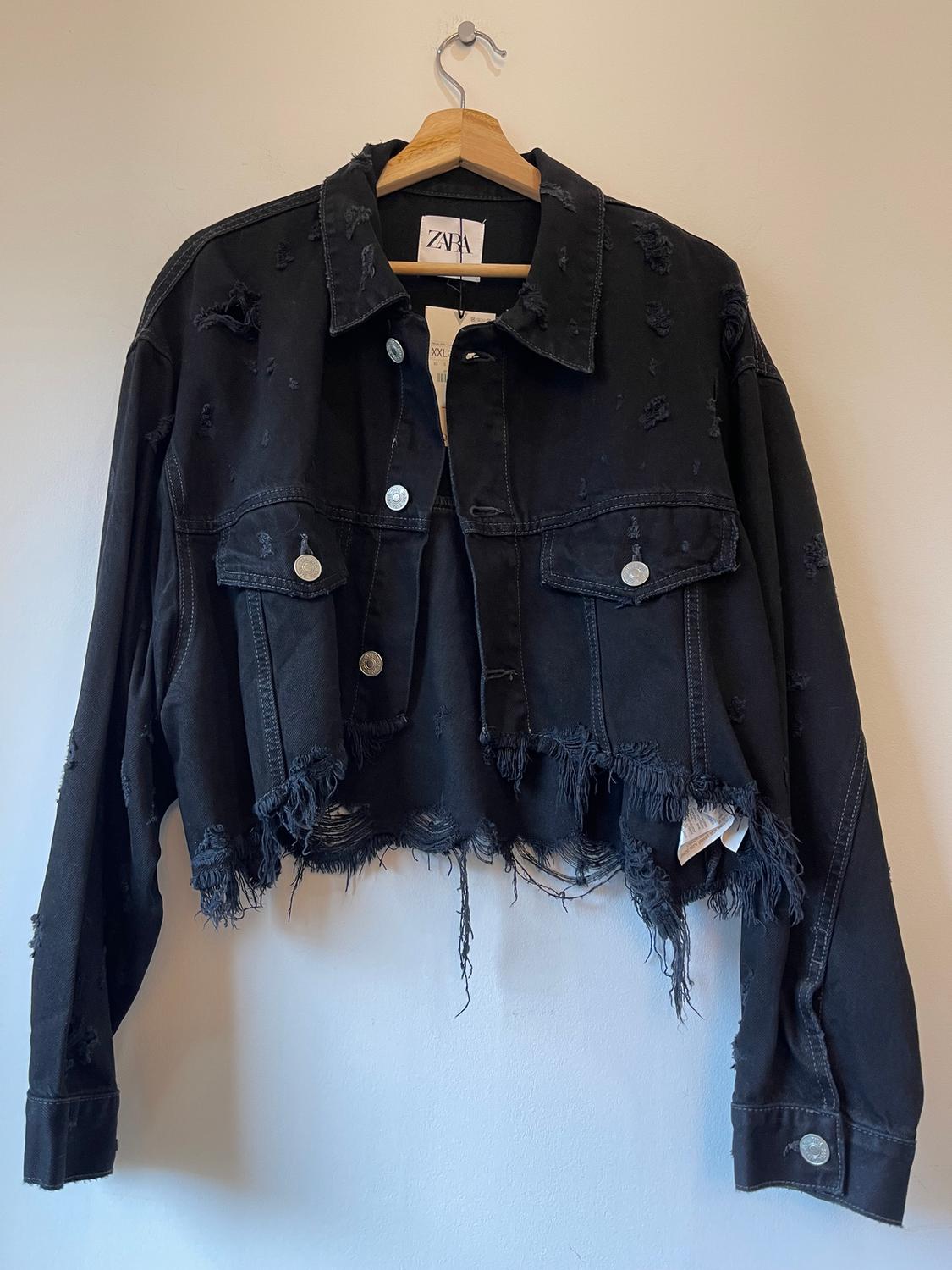 Worn black jacket with metal buttons and frayed hem, hanging on a wooden hanger. Visible label: ZARA.