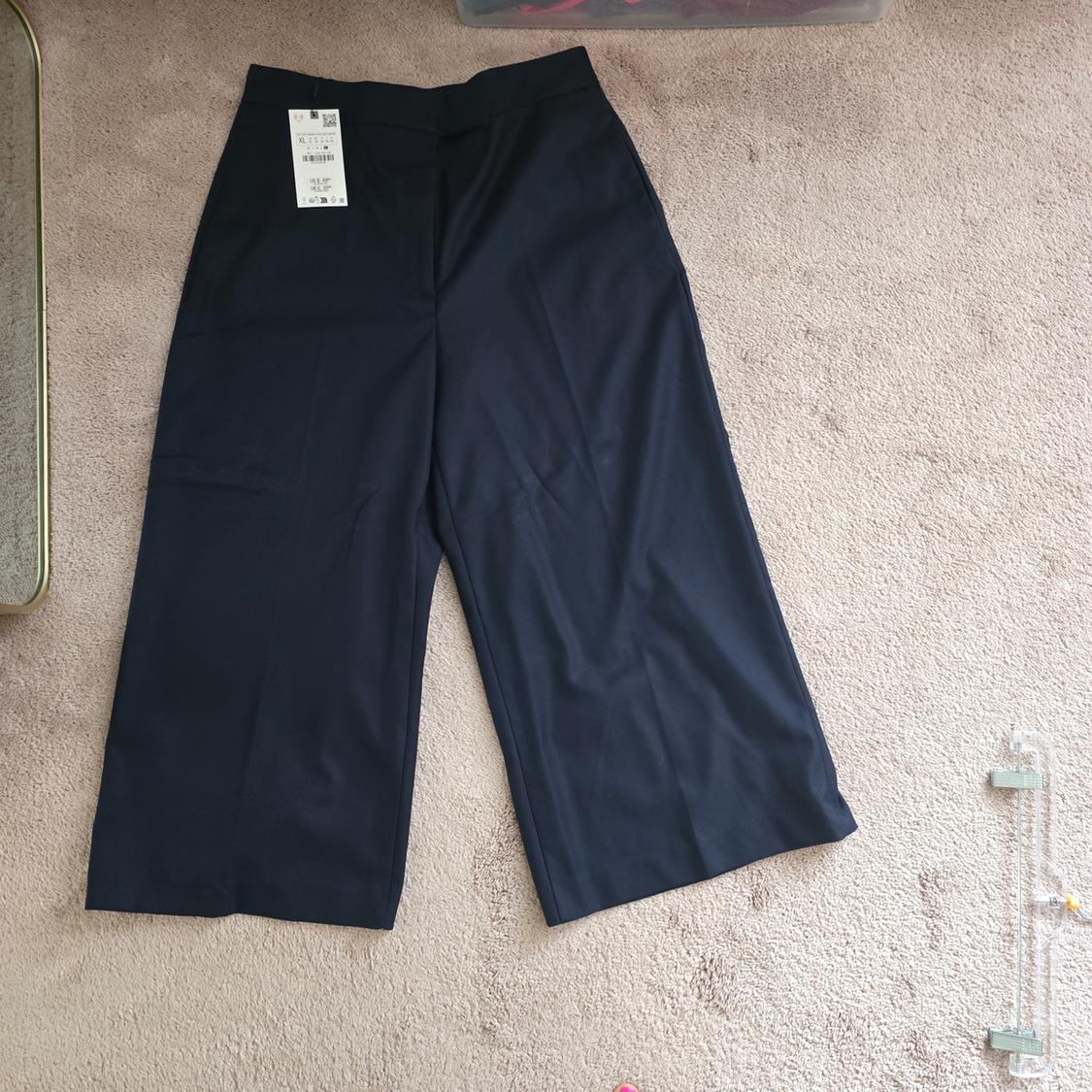 Navy blue wide-leg pants on a beige carpet, white tag hanging from the visible left side with price and code details.
