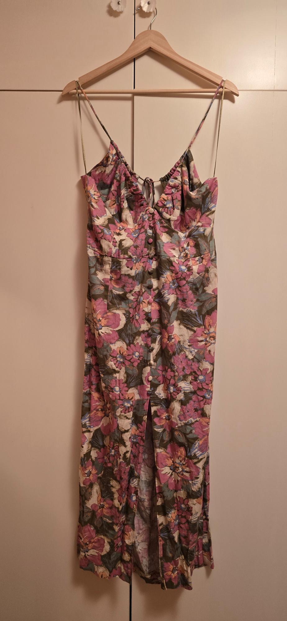 Floral print strappy dress with a V-neck, front buttons and a split. Hanging on a wooden hanger on a light-coloured wardrobe.