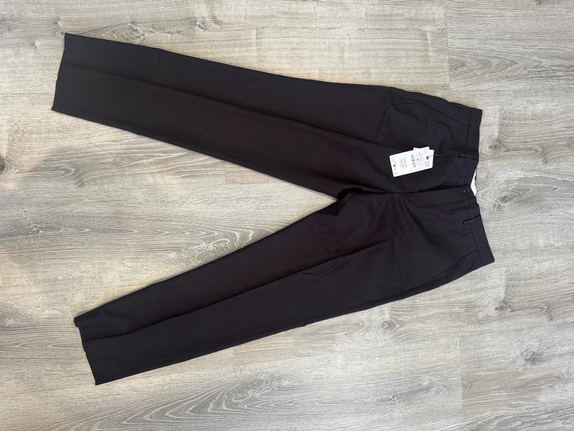 Black formal trousers with a pressed crease and a label, laid out on a grey wooden floor.