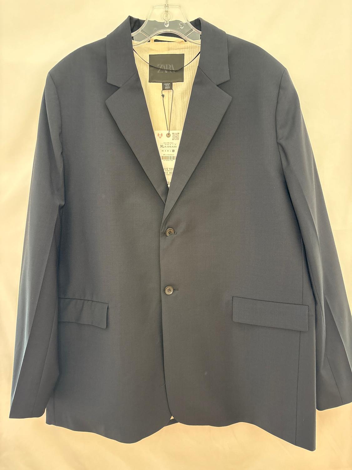 Black suit jacket hanging on a clear hanger, with a visible tag inside. Light background.