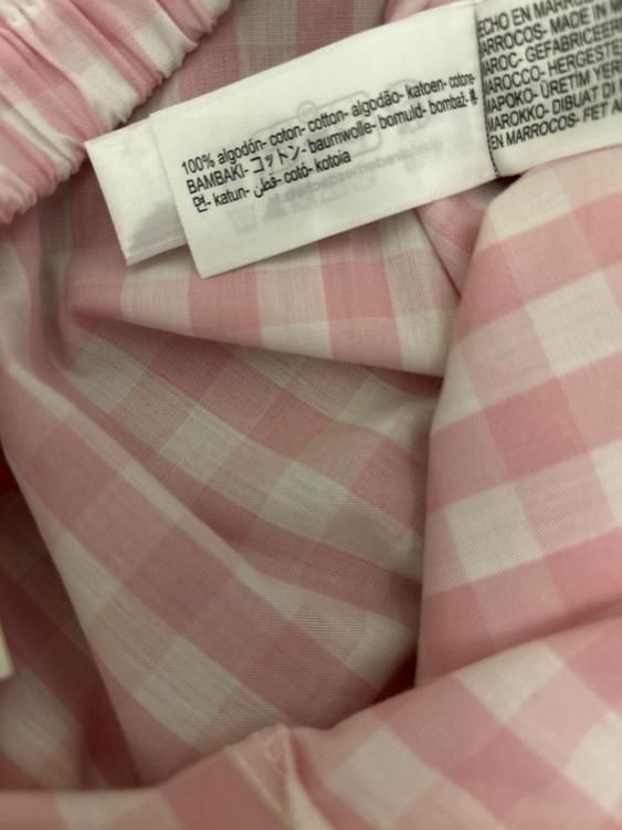 100% cotton fabric label in multiple languages on pink and white checked fabric. Visible text: "100% cotton".
