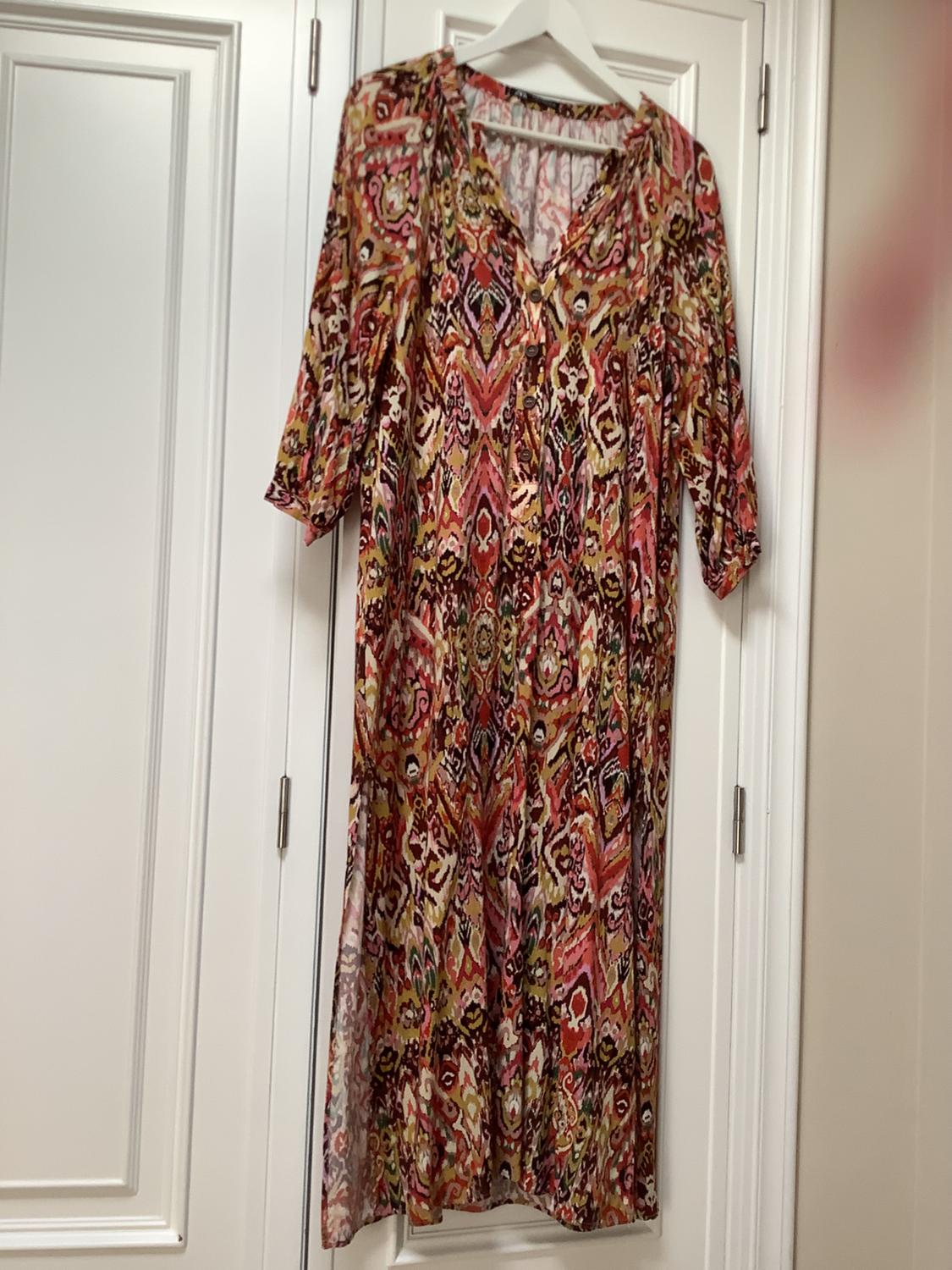 Long dress with colourful print hanging on a white hanger over a white door. Three-quarter sleeves and V-neck.
