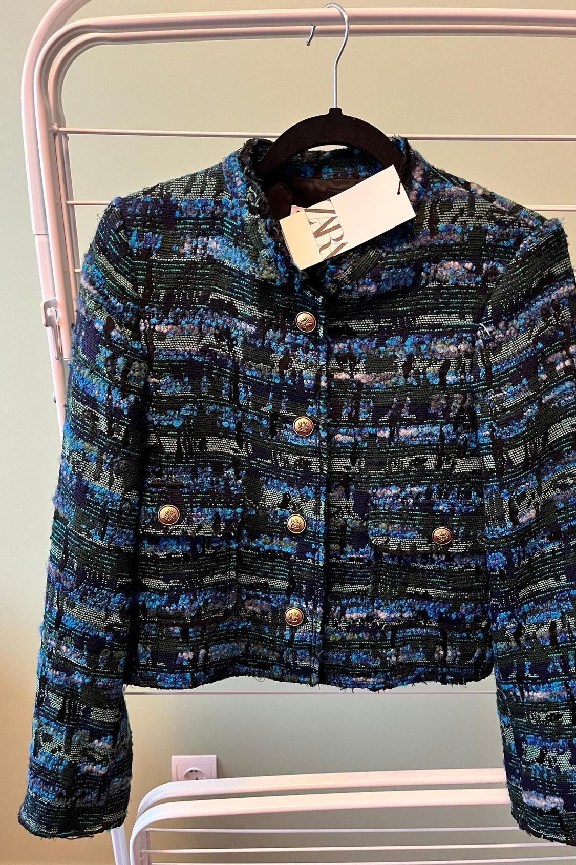 Front view of a short jacket with blue and black print, gold buttons and front pockets.