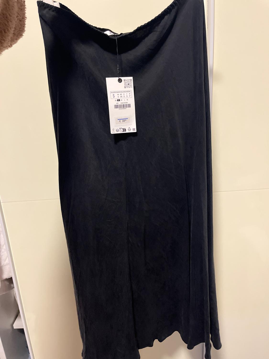 Black skirt hanging with visible tag showing size S and price of €39. White and beige background.