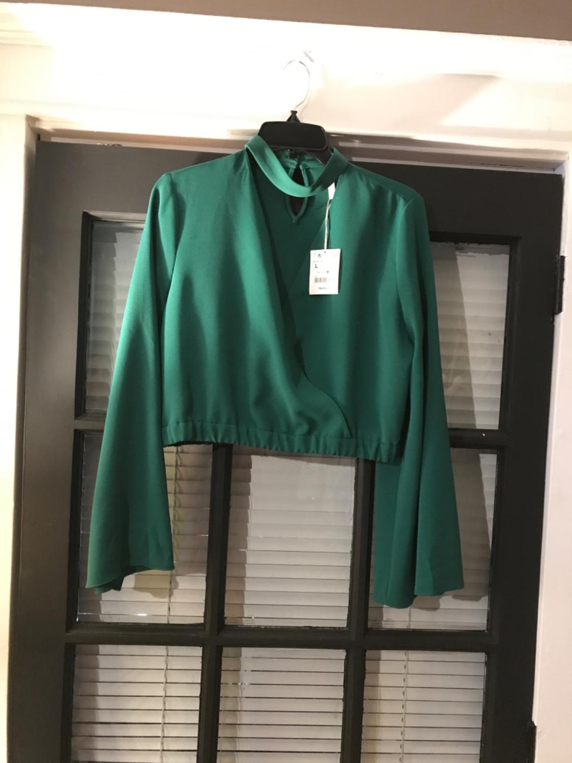 Front view of a green blouse with a high neck and long sleeves, elasticated waist, visible label.