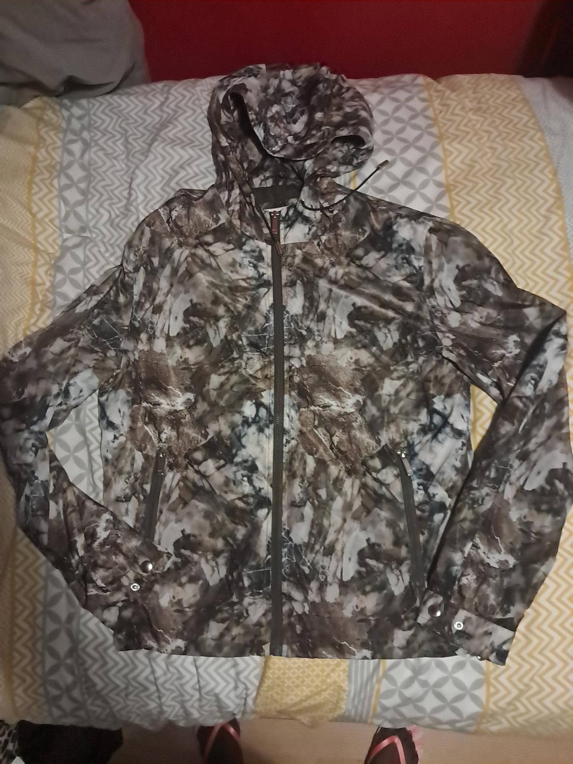 Abstract print hooded jacket in shades of brown, grey and white, with a central zip, laid out on a bed.