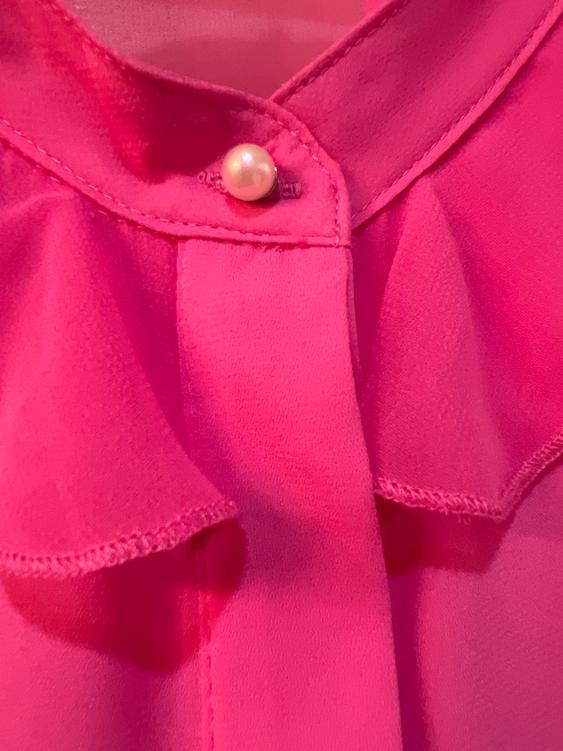 Detail of a pink blouse with a collar and pearl button. Lightweight fabric with visible seams and soft pleats.