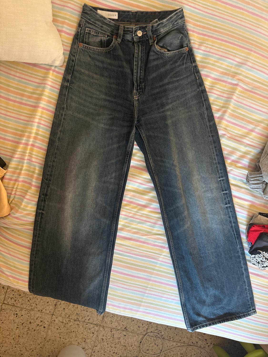Dark blue denim straight-cut jeans, placed on a bed with a multicoloured striped bedspread.