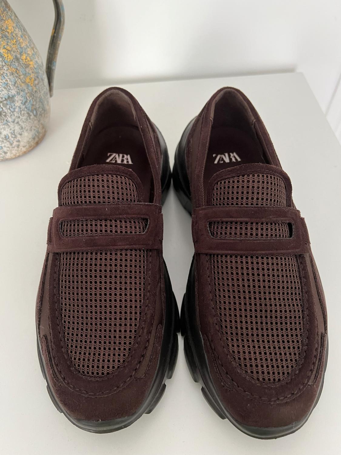 Brown mesh shoes with black soles on a white surface. Visible text: "ZARA" on the inside of the shoes.