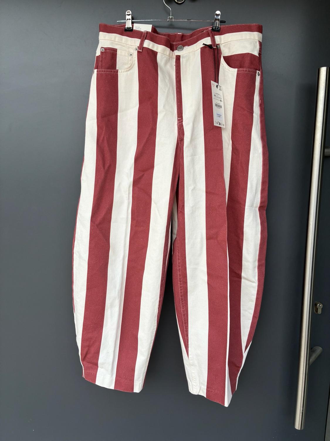 Wide trousers with red and white vertical stripes hanging on a metal hanger in front of a dark grey door.