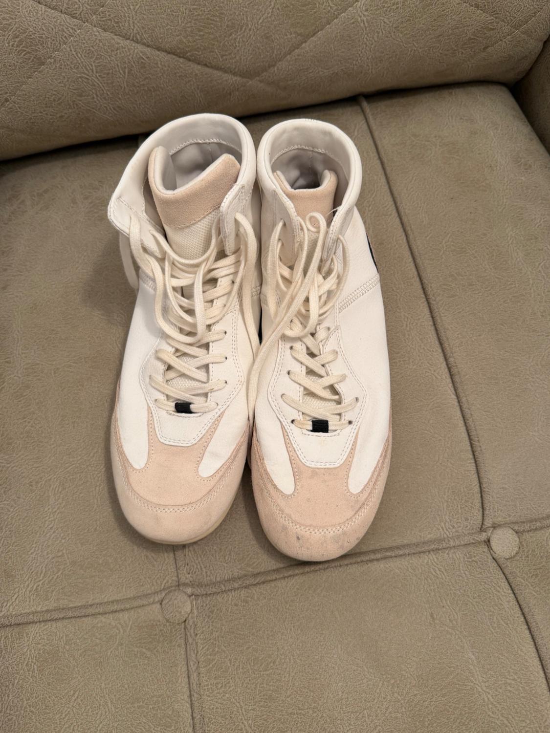White and beige high-top trainers with laces, resting on a textured cushioned seat. Casual and relaxed style.