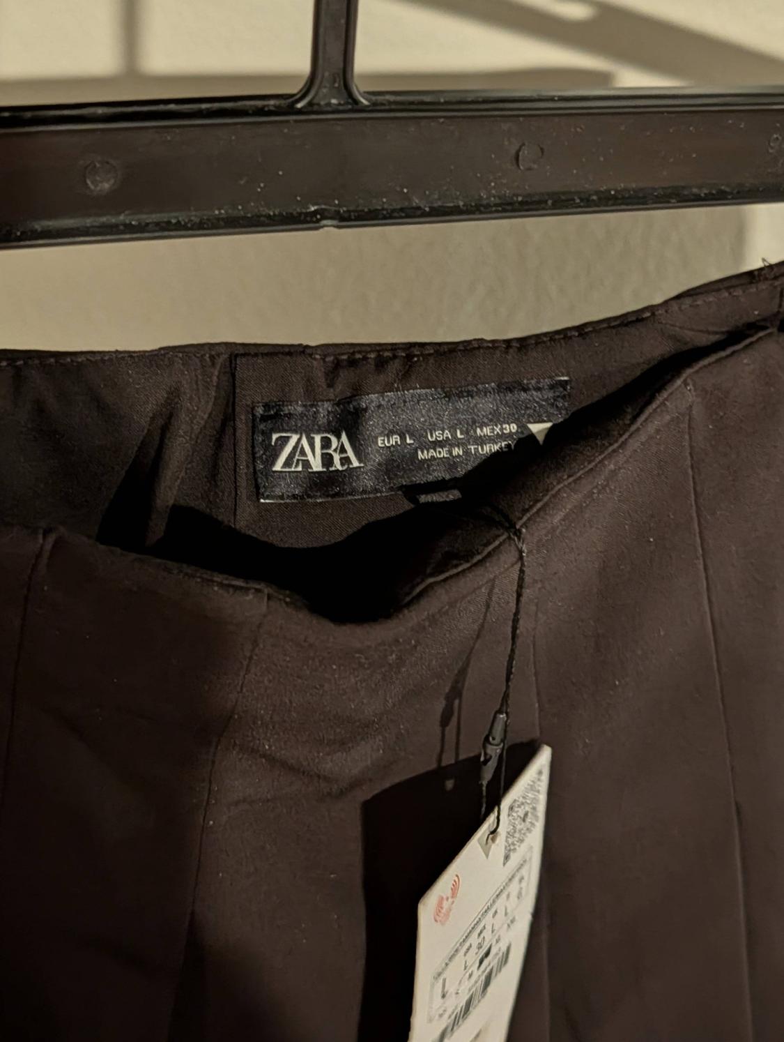 Zara black pants tag hanging on a hanger. Visible text: "ZARA, EUR L, USA L, MEX 30, MADE IN TURKEY".