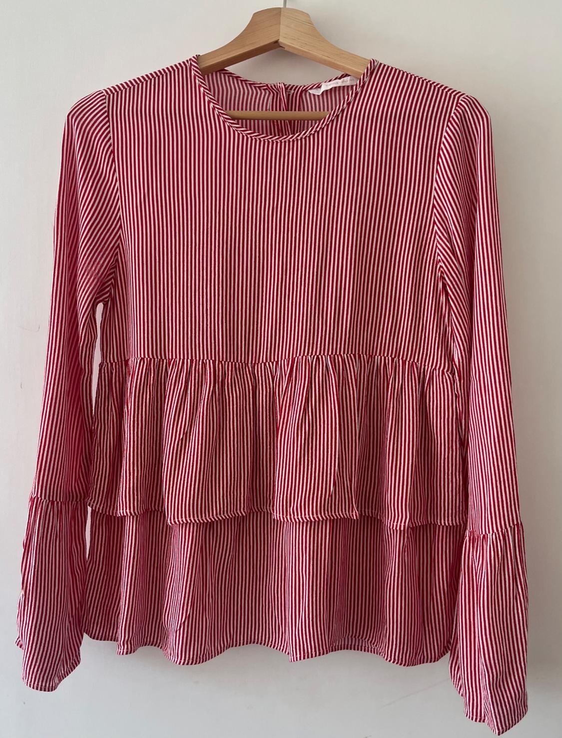 Red and white vertical striped blouse, round neckline, ruffled sleeves and hem. Hanging on a wooden hanger against a white background.