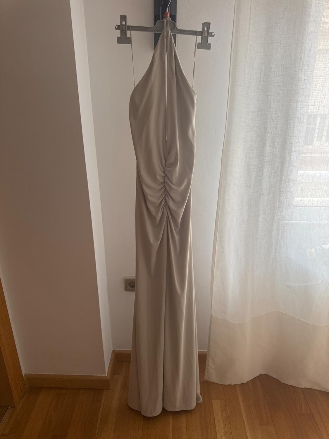 A beige maxi dress hanging on a clothes hanger, with a ruched design on the front, in a room with a wooden floor and a white curtain.