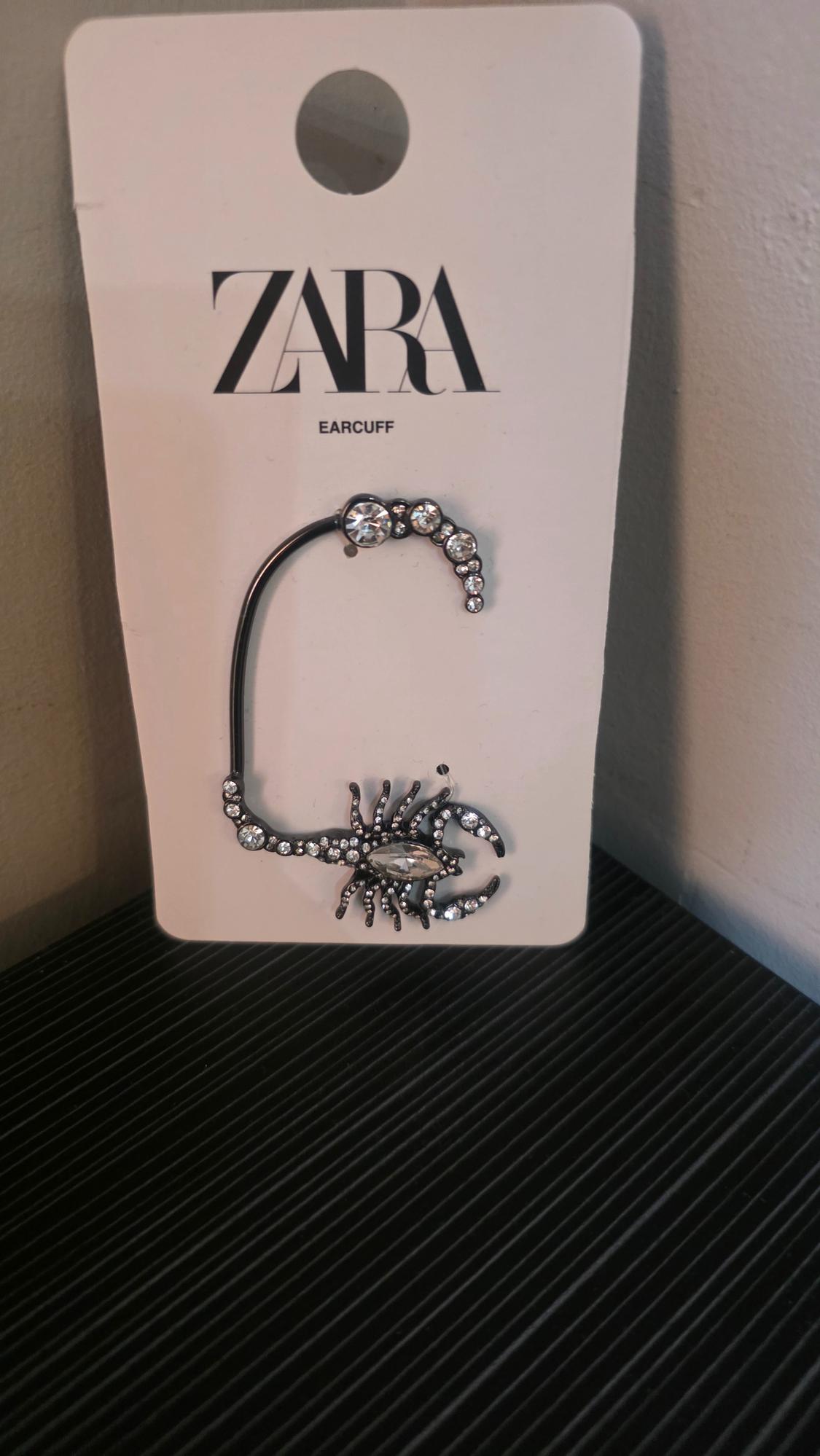 Scorpion design ear cuff with crystals on a white label with the text ZARA EARCUFF, resting on a black surface.