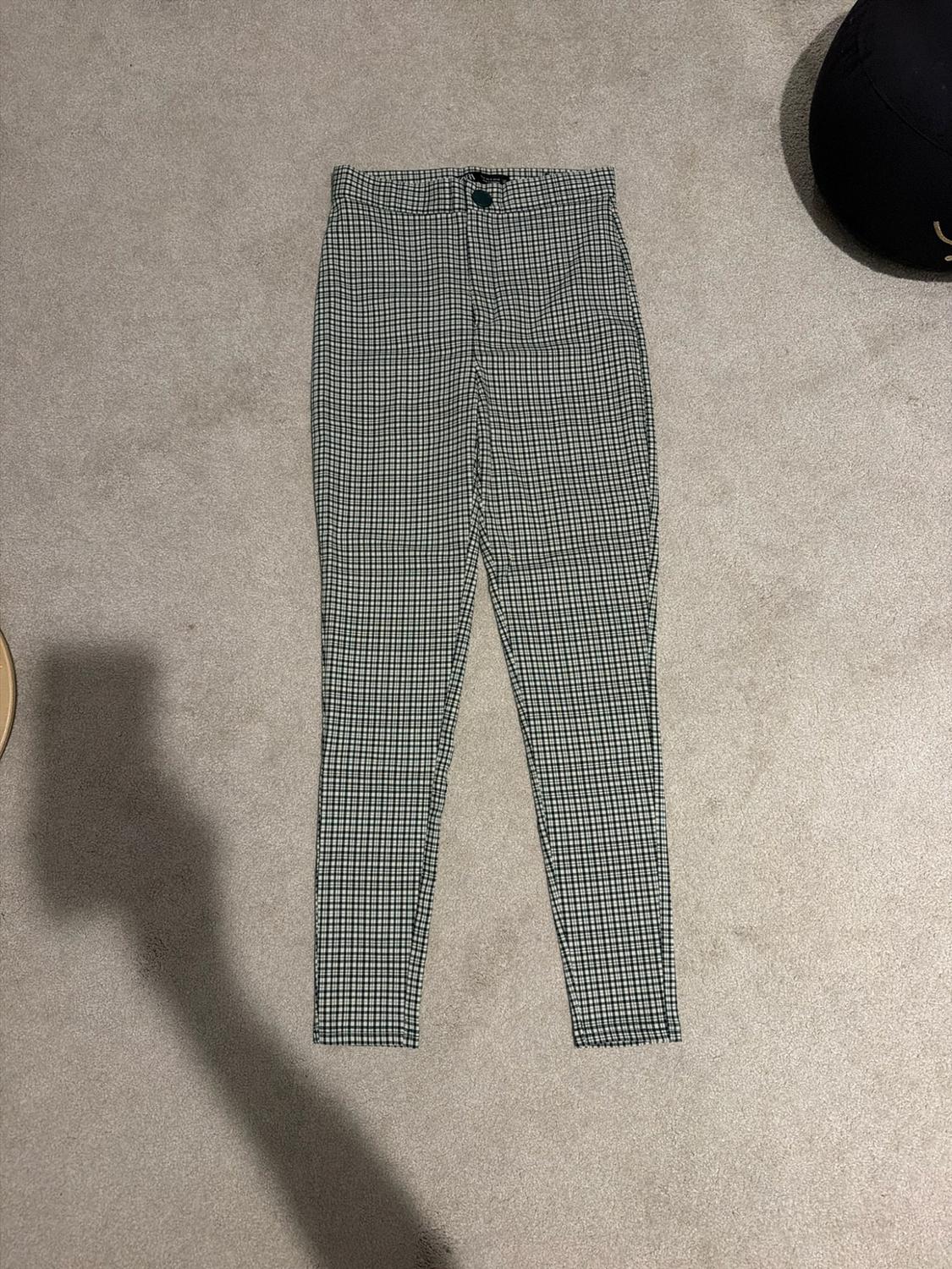 High-waisted, tight-fitting black-and-white checked trousers on a grey carpet. The shadow of the person taking the photo stands out.