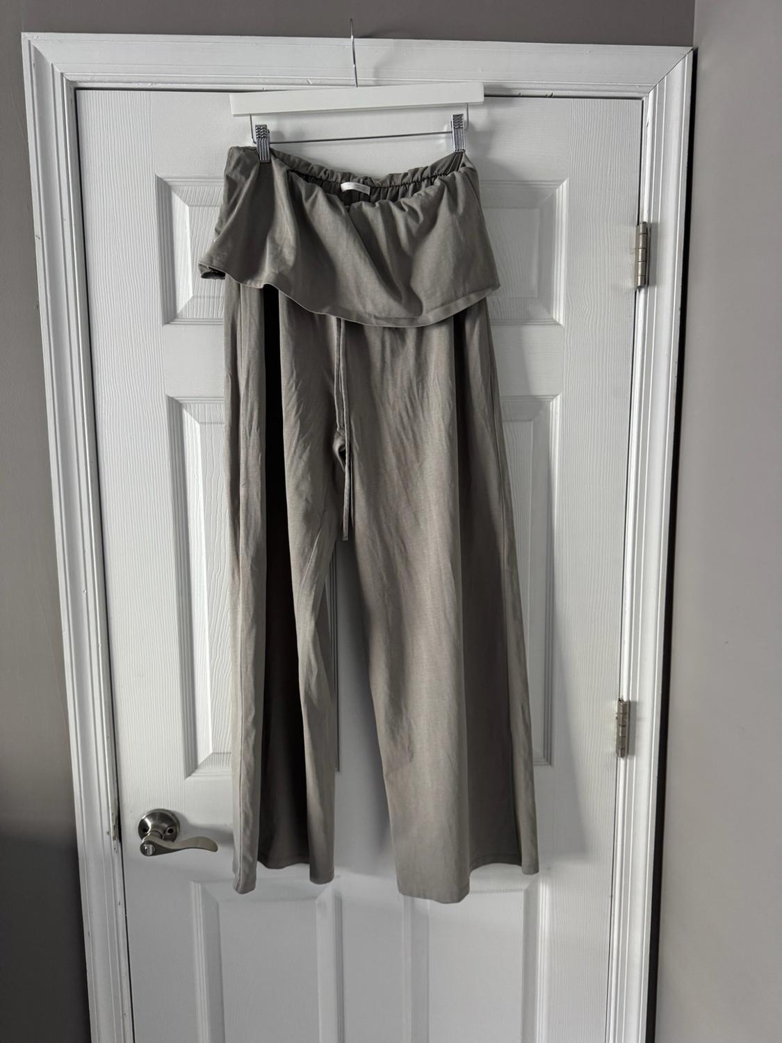 Wide gray pants with a folded ruffle-style waistband, hanging on a hanger over a white door. Casual and relaxed style.