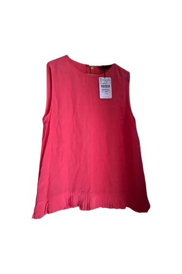 Front view of a pink sleeveless blouse with a visible label and a pleated hem.