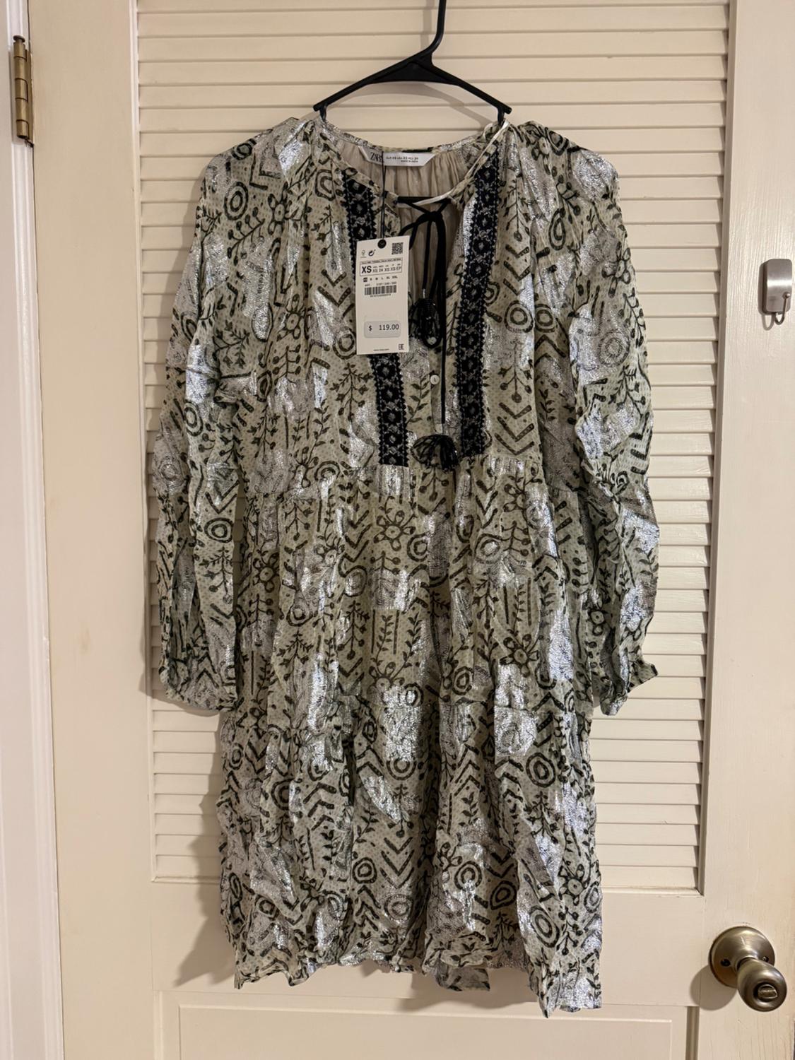 Printed dress in silver and black tones hanging on a hanger. Visible tag with price of $119. Door in the background.