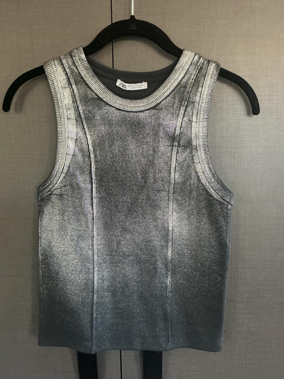 Metallic silver sleeveless top with a ribbed crew neck, hanging on a black hanger against a neutral background. ZARA label.