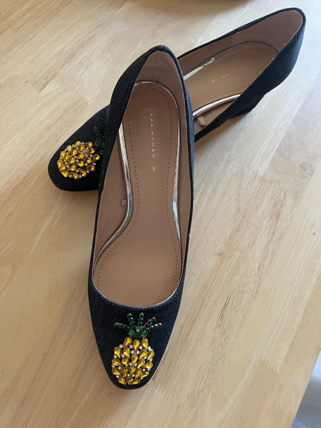 Detail of black shoes with pineapple embellishment on the toe.