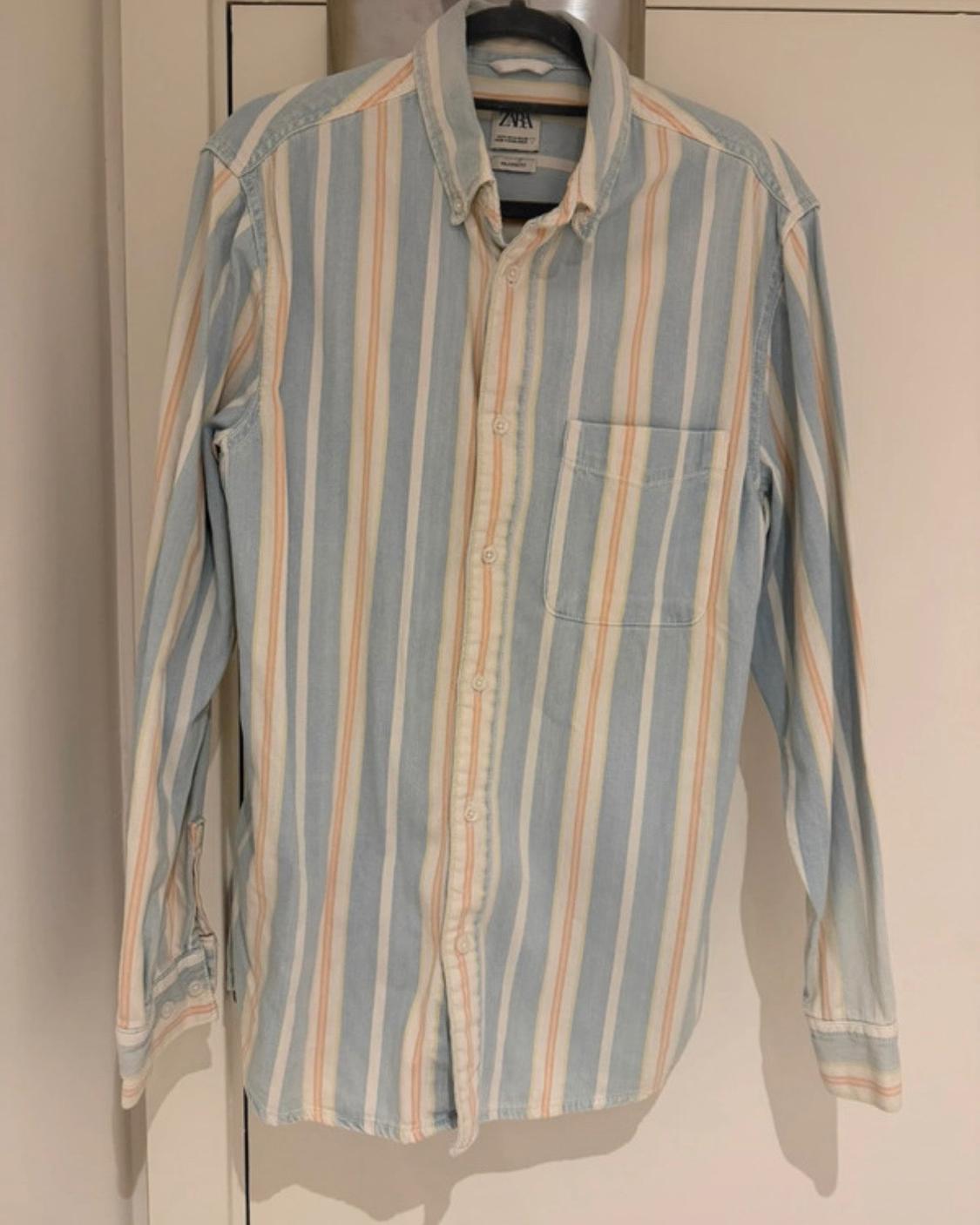 Light blue, white and orange vertical striped long-sleeved casual shirt hanging on a hanger. Front pocket and Zara label.