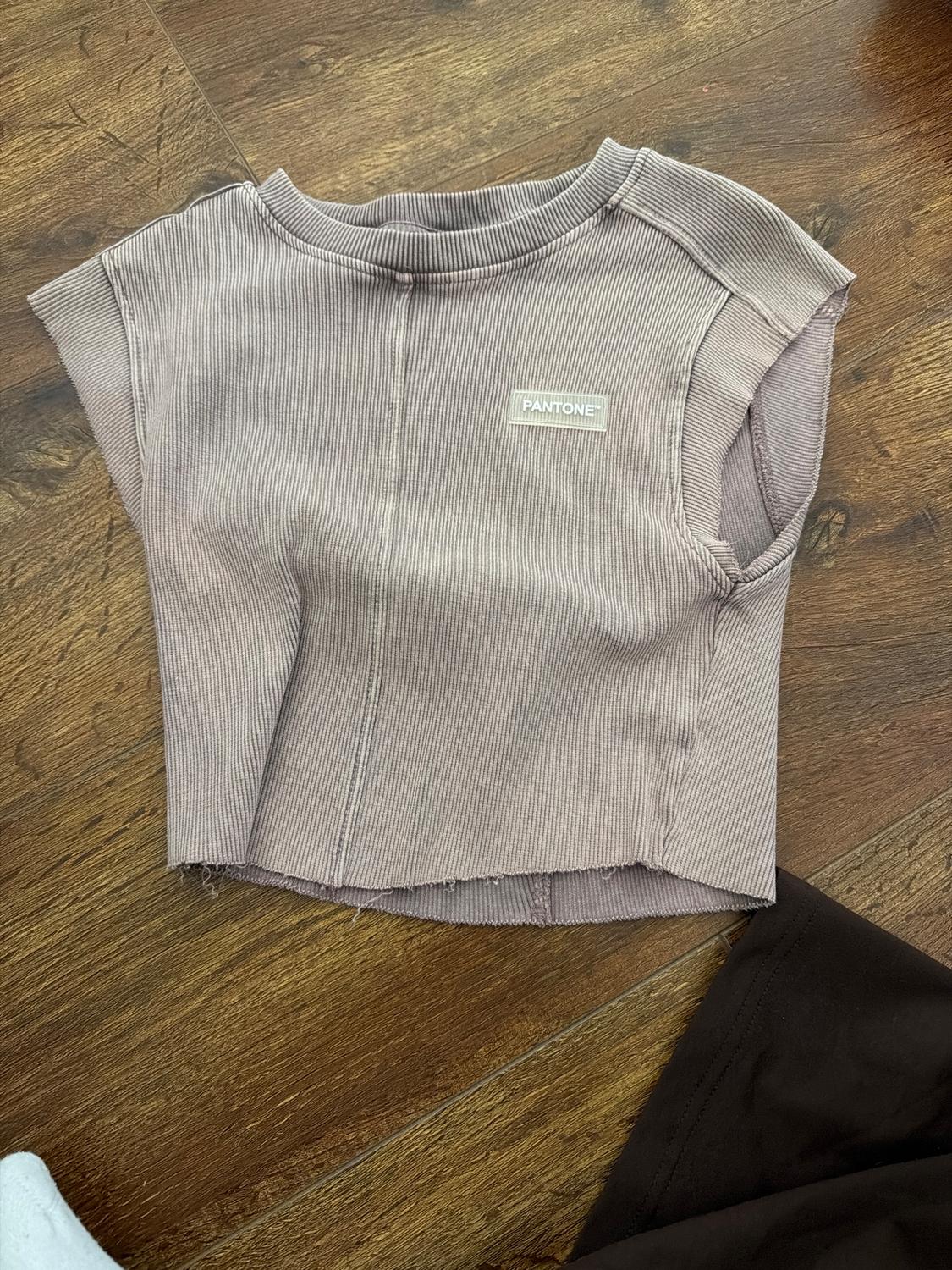 Beige ribbed vest top with a "Pantone" label on the chest, on a wooden floor.